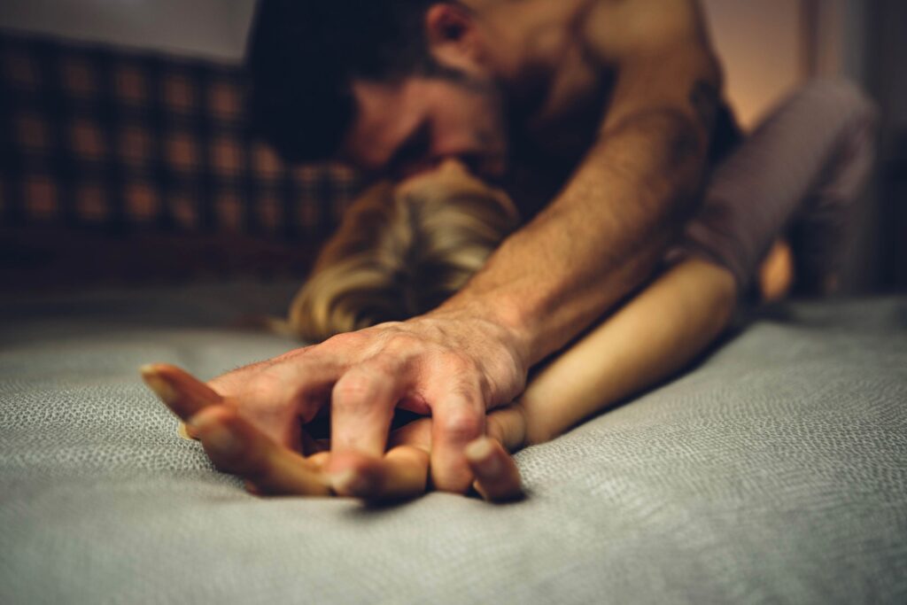 Close up image of intimate couple holding hands while having sex on bed